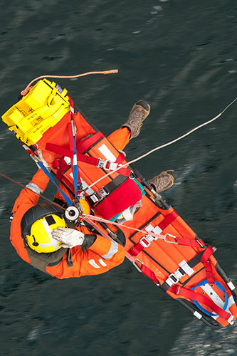 Image of a SAR winchman on the cable with a stretcher